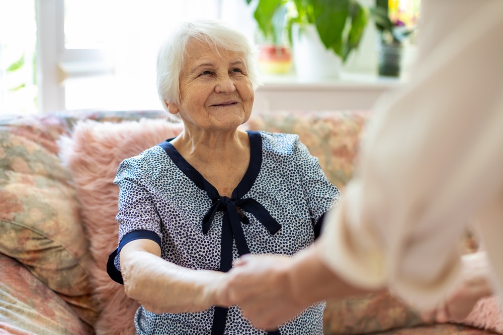 Smiling senior woman looking at and holding hands with younger woman out of focus