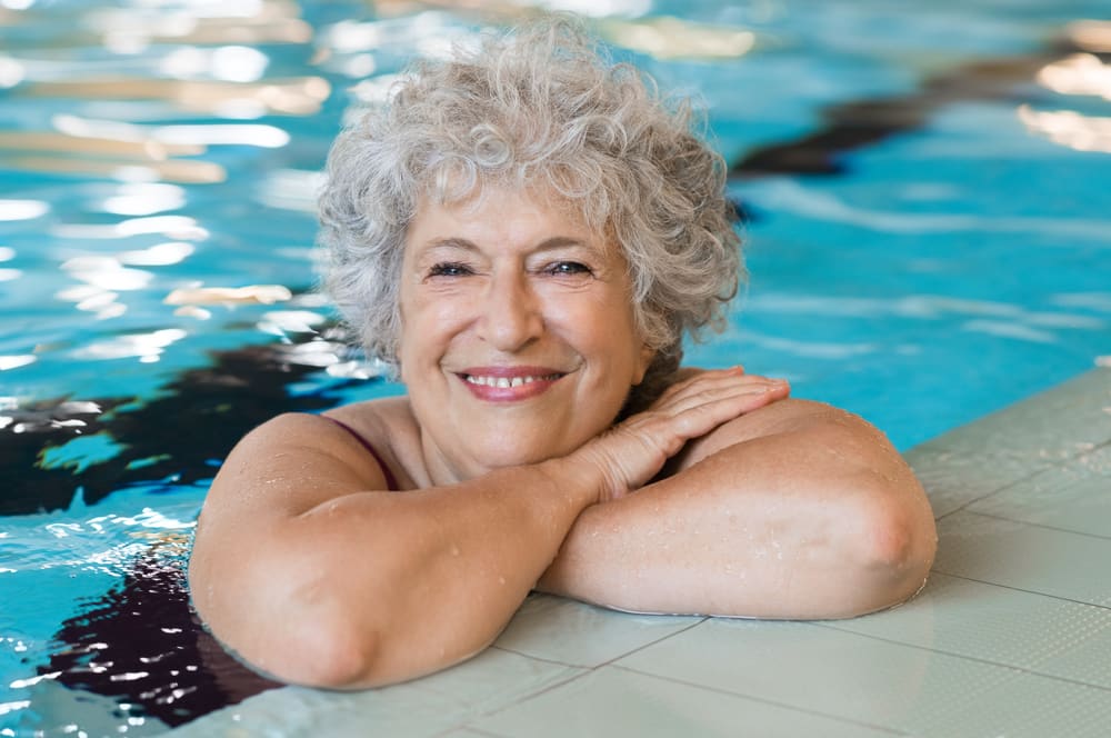 Senior woman smiling, leaning on edge of pool