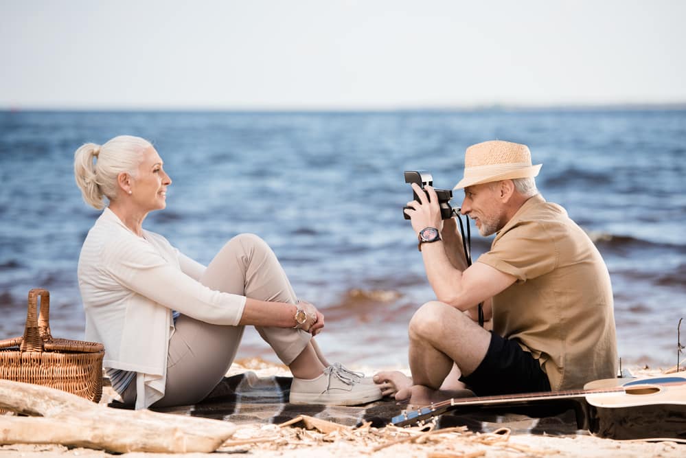 Senior man taking photo of senior woman on the beach