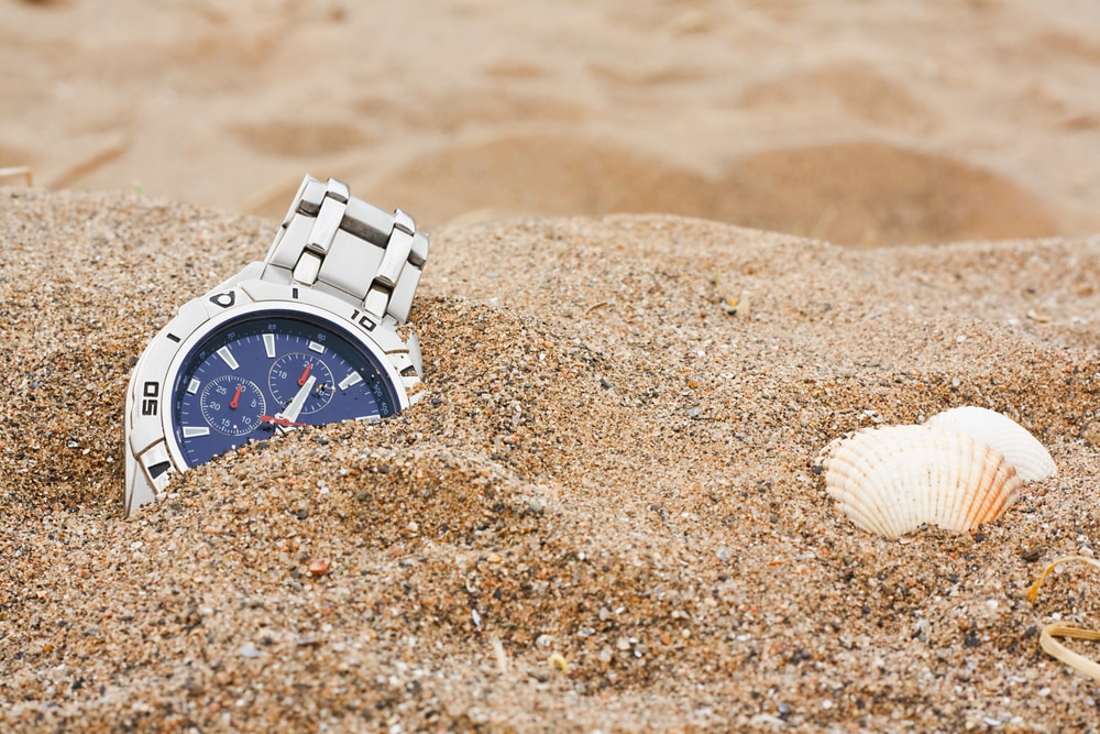 wrist watch in sand at the beach beside seashell