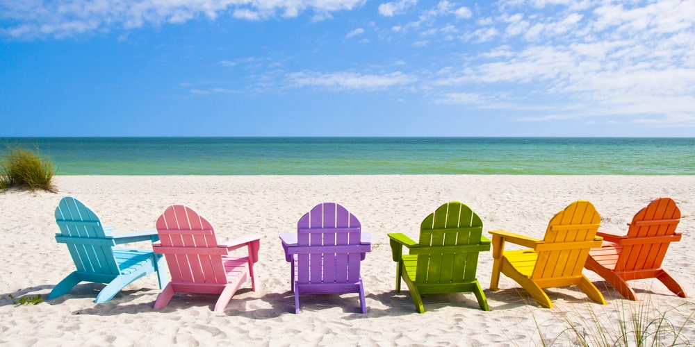 Colorful adirondack chairs in a row on sandy beach
