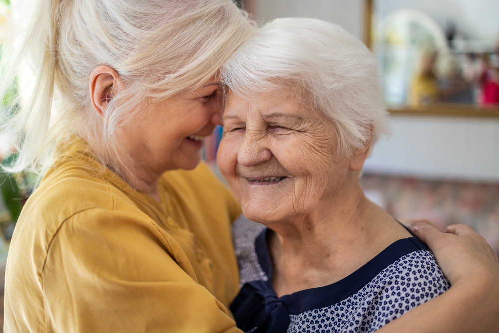 Woman hugging senior woman, both smiling