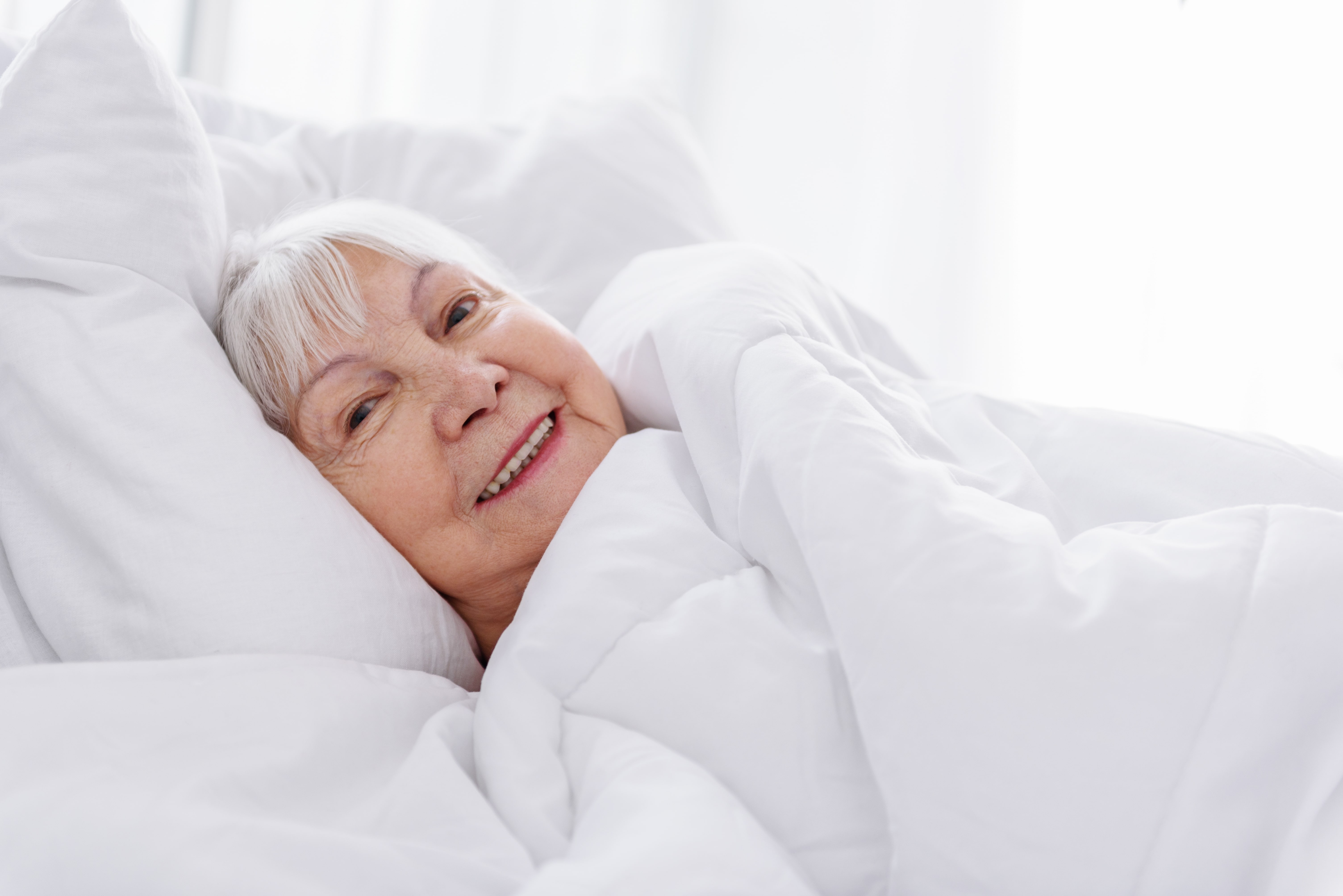 Smiling senior woman beneath covers in bed