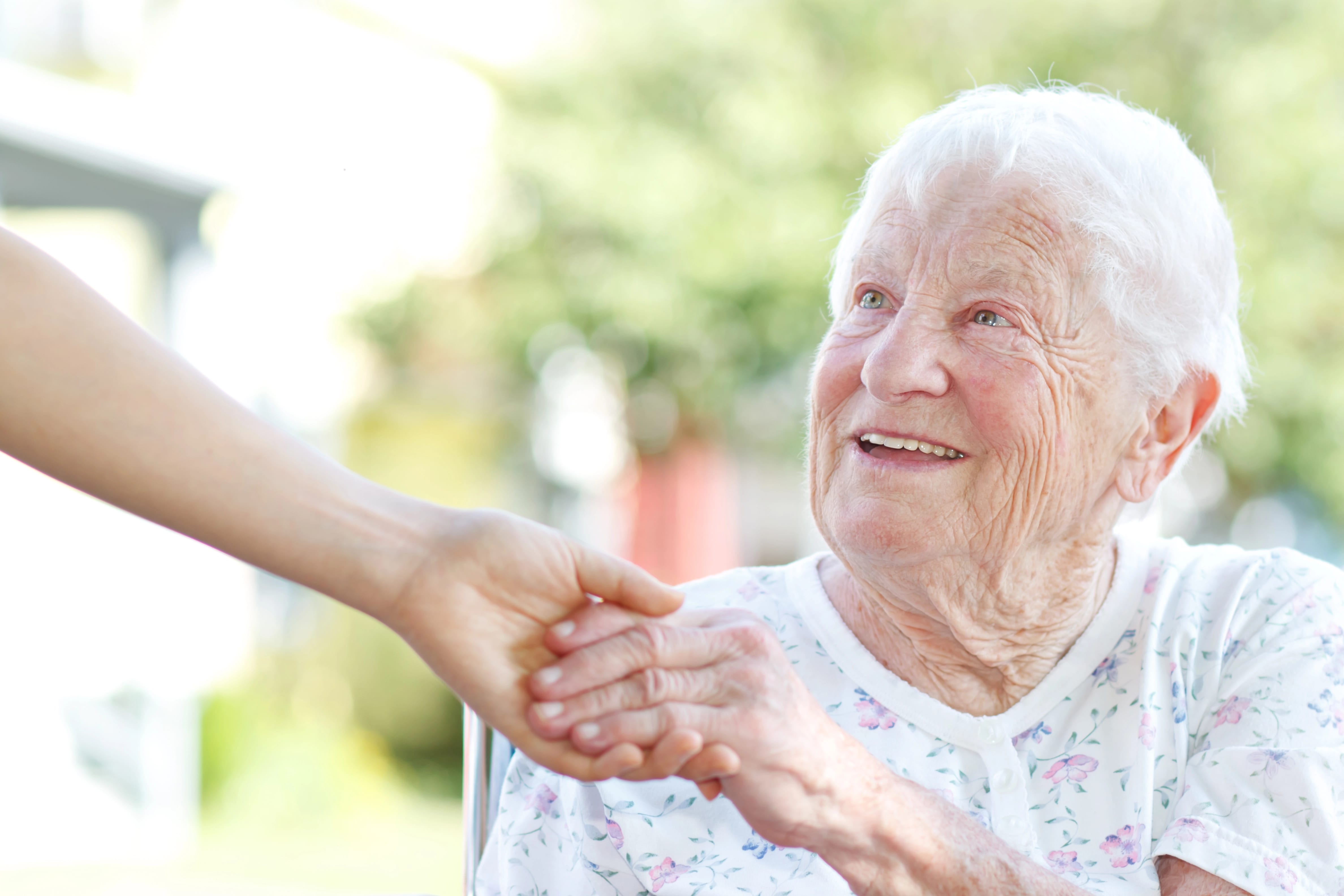 Senior smiling up at younger person and shaking their hand